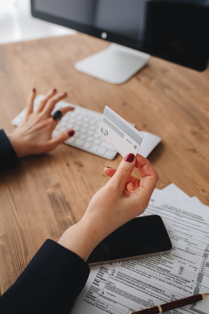 Womans hand with credit card and manicured nails typing on keyboard. Modern business setup.
